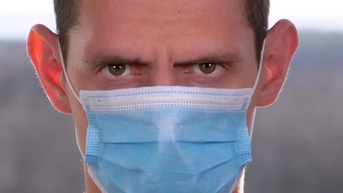 Young Man in a Medical Protective Face Mask Looking at the Camera on the Street Background