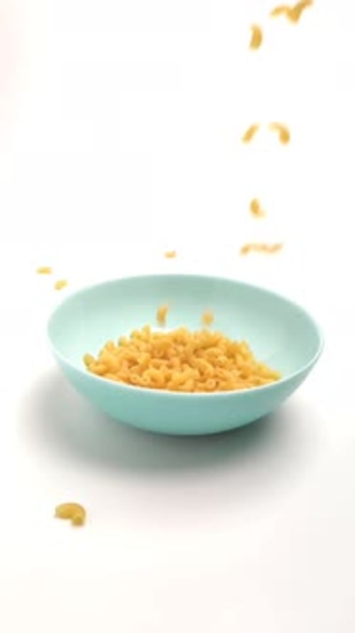 Wheat Pasta Falls on a Blue Plate on a White Background. Close-up, Slow-motion