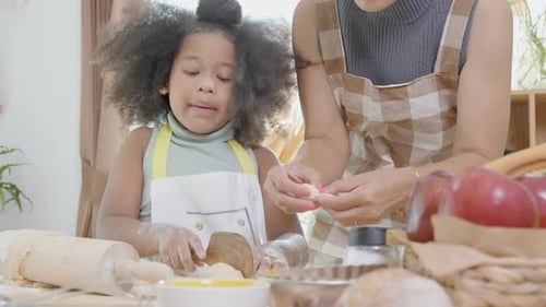 African America family with mother wearing apron rolling thresh flour for cooking with daughter.