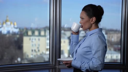 Woman Drinking Coffee by Window in City Building