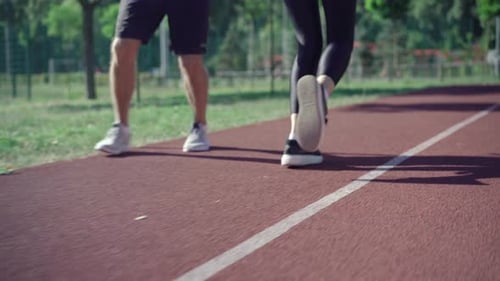 Beine von unkenntlich fitten Männern und Frauen, die auf einer sonnigen Strecke im Freien laufen. Sportliches kaukasisches Paar