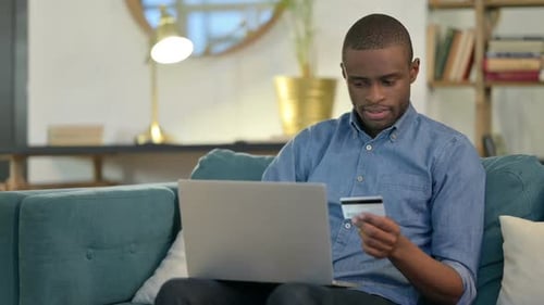 Online Shopping Success on Laptop By Young African Man on Sofa