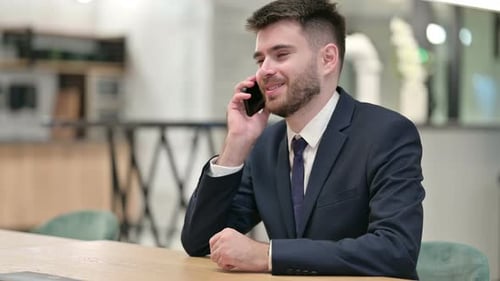Cheerful Young Businessman Talking on Smartphone in Office