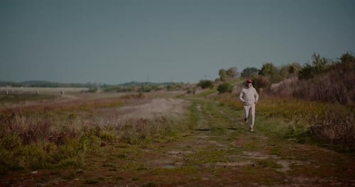 Man Running on Dirt Path Through Grassy Field