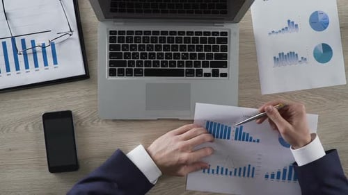 Mann analysiert Grafiken und gibt Daten auf einem Laptop im Büro ein, Ansicht von oben
