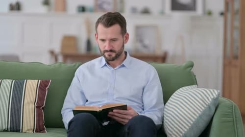 Man Reads Book on Couch at Home