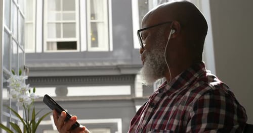 Man Using Smartphone With Headphones by Window