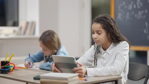 Fröhliches afroamerikanisches Schulmädchen surft Internet-Messaging online auf Tablet mit Unschärfe