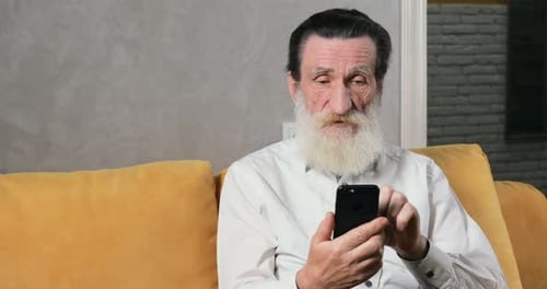 Senior Man Using Smartphone on Couch Indoors