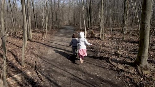 Two little children running down a forest path, slow motion.