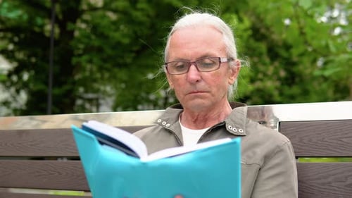 Senior Man Reading Book Sitting on Bench in Park