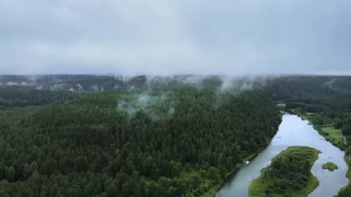A mystical fog rises over taiga. Hills overgrown with pines on cloudy rainy day