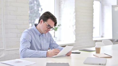 Serious Working Young Man Doing Paperwork in Office