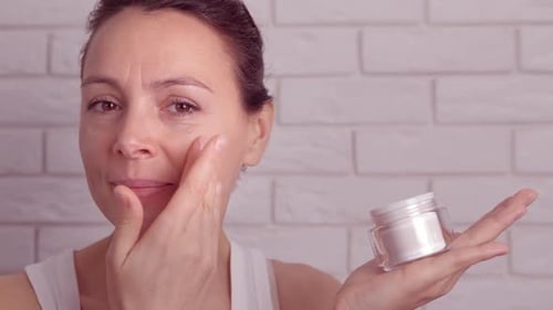 Woman Applying Moisturizing Face Cream Indoors