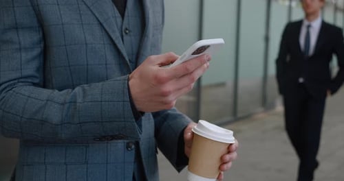 Man Using Phone with Coffee Outside Office Building