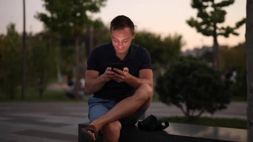 Man Using Mobile Phone Sitting on Beach in Park