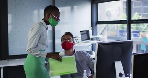 Diverse male and female office colleagues wearing face masks discussing at modern office