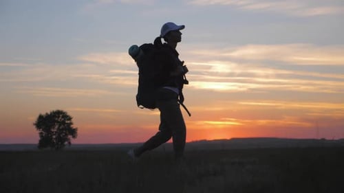 Woman Walking With Backpack in Rural Field at Sunset