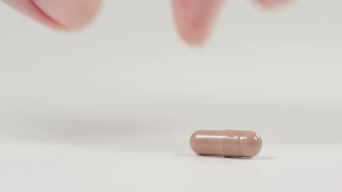 Finger Taps Small Pink Capsule on White Surface