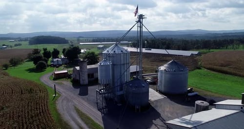 Poussée aérienne au-dessus des champs de maïs jusqu'aux silos à grains et s'élevant au-dessus avec vue sur le drapeau américain battant un