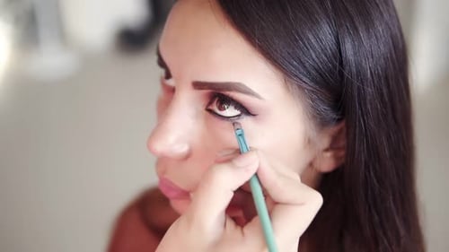 Imágenes de gran ángulo de un maquillador irreconocible aplicando y mezclando el párpado inferior de una modelo con