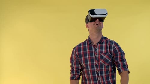 Homme aux cheveux noirs utilisant des lunettes de réalité virtuelle debout sur fond jaune