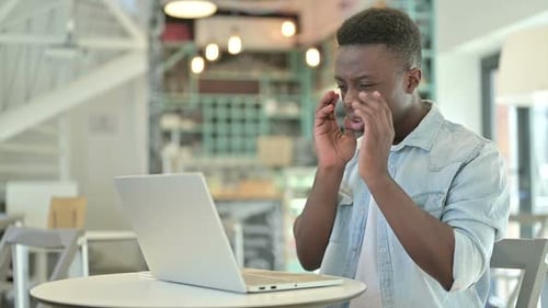 Young Adult Using Laptop Looking Stressed in Cafe
