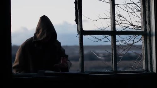 Silhouette Man in Dark Cloak with Hood on Head Against Sky Twilight Time