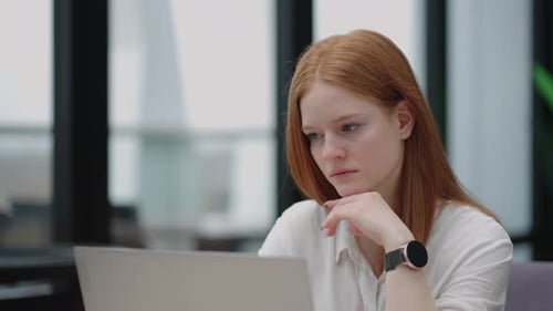 Thoughtful Concerned Redheaded Woman Working on Laptop Computer Looking Away Thinking Solving