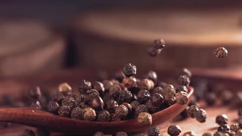 Black Peppercorns Falling into a Wooden Spoon