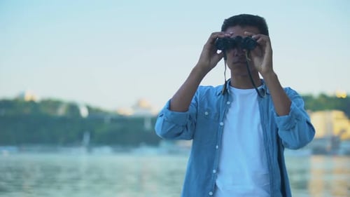 Neugieriger Teenager, der Zeit am Flussufer verbringt und durch ein Fernglas schaut