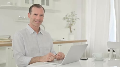 Smiling Man Working on Laptop in Bright Kitchen