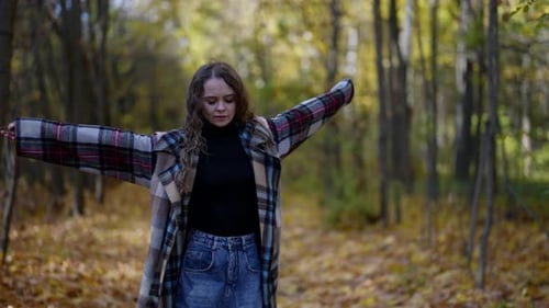 a Blonde with Long Hair and in a Plaid Coat Spreads Arms and Walks Backwards Through the Autumn Park