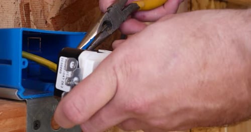 A construction worker using pliers to install an electrical outlet with wires in the framing of a ne