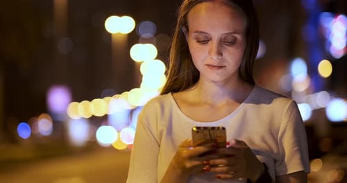 Young Girl in the Night City Writes Text Messages in a Smartphone