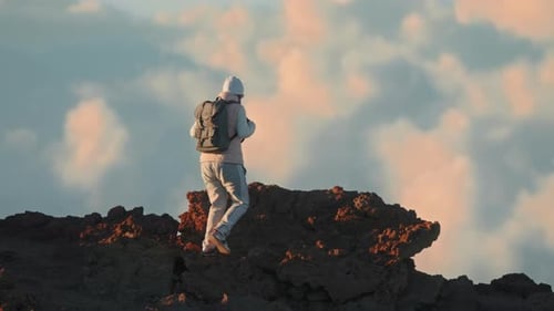 Touriste escaladant le rocher d'une montagne volcanique dans un paysage nuageux pittoresque au coucher du soleil cinématographique