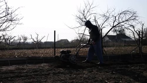 Man Farmer Working in the Garden Plows with Garden Tiller