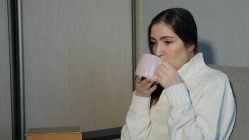 Beautiful Girl Drinking Tea and Reading a Book on the Sofa