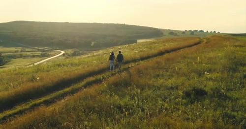 Expanses of Meadows and Fields Two Tourists Walk with Backpacks on Foot
