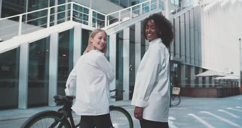 Deux jeunes femmes en tenue professionnelle, avec un vélo dans un quartier d'affaires