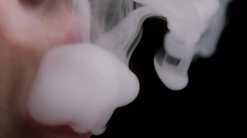 Gros plan de la belle jeune femme fumant le narguilé ou la cigarette dans le studio sombre vue côté de la femme