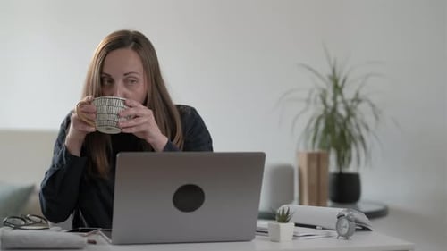 Woman Works on Laptop, Drinks Coffee at Home