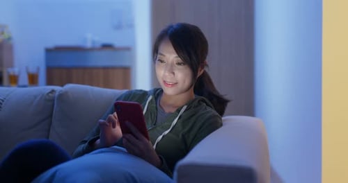 Asiatische Frau benutzt Handy sitzt abends zu Hause auf dem Sofa