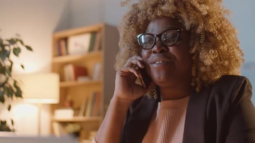 Cheerful Woman Talking on Smartphone in Warmly Lit Office