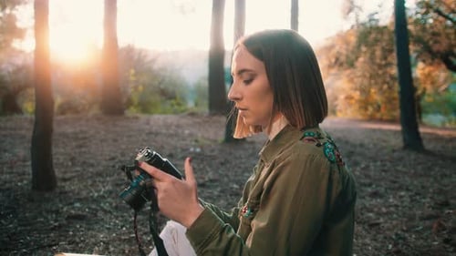 Woman Examining Camera in the Woods at Sunset