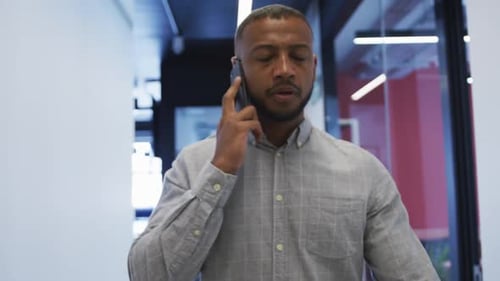 Mixed race businessman walking talking on smartphone checking his watch in modern office