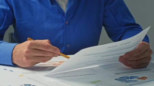 Closeup Businessman Takes Notes in Documents Graphs and Works Behind a Laptop