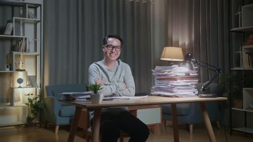 Asian Man Crossing Arms And Smiling To Camera While Working With Documents At Home