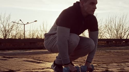 Man Doing Shoulder Raises with Dumbbells at Sunrise