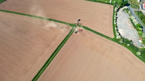 Aerial footage of a farmers field being plowed by a tractor in the summer time,